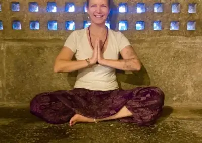 a woman sitting cross legged in front of a stone wall with blue lights